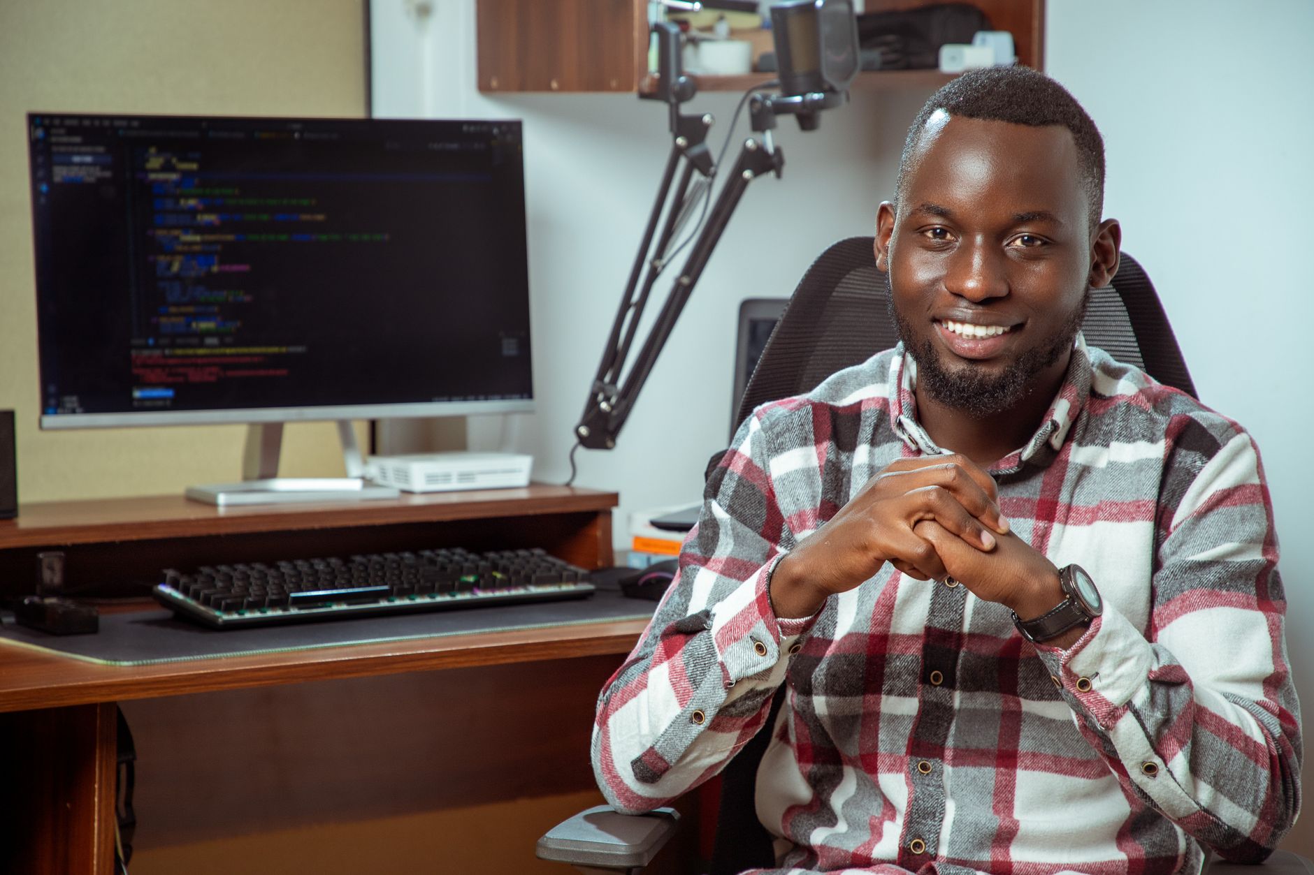 Retrato de un programador sonriente frente a una pantalla de ordenador con código.
